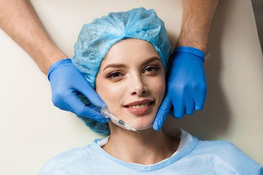 Lips augmentation injections for attractive girl on white background. Plastic surgeon does injection in lip in medical clinic.