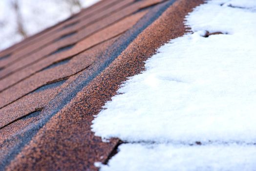 Red shingles. The roof of a house made of shingles is covered with snow in winter, close-up. Frost resistance and elasticity of bituminous tiles in severe frosts