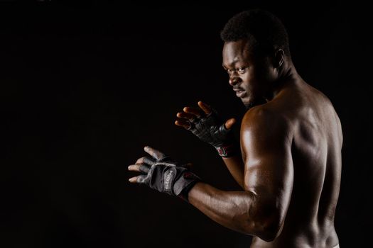 Athletic african fighter on black background. Dark skinned undressed man shows a fight. Advert for sport club and gym. Professional boxing and karate