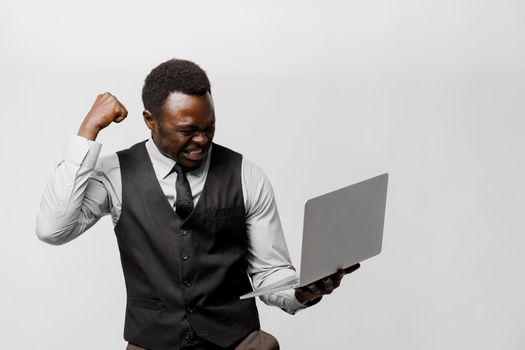 Winning a prize in on-line lottery. Black man uses laptop and wins a money. Successful happy bearded african in white shirt and black vest and tie