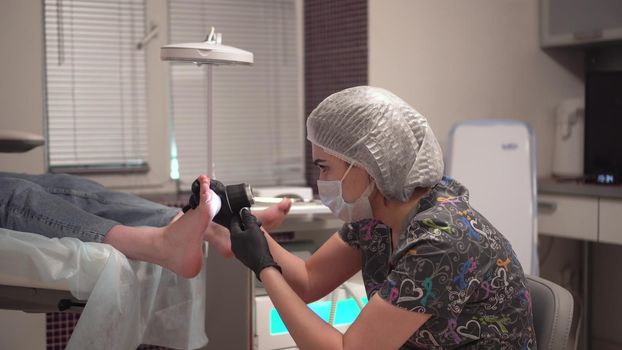 The pedicurist looks at the patient's foot through a portable microscope. Procedure at the podiatrist in the salon. 4k