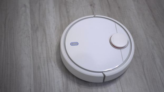 A white robot vacuum cleaner rides on a white parquet floor. The robot with artificial intelligence determines the space and cleans the floor. 4k