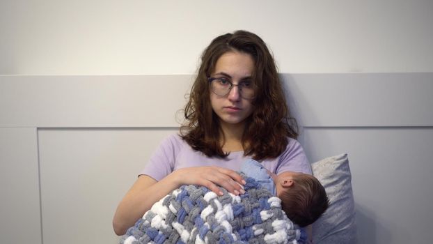 An exhausted young mother cradles a child in her arms in bed. A woman with a frenzied tired look with a newborn in her arms. 4k