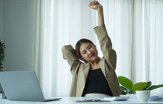 Young Asian businesswoman stretching arms raised relaxing at the office..