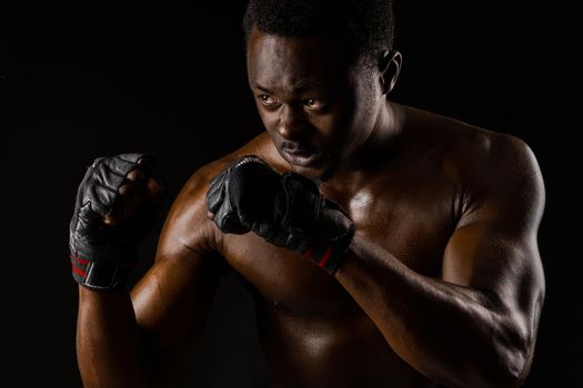Athletic african fighter on black background. Dark skinned undressed man shows a fight. Advert for sport club and gym. Professional boxing and karate