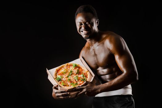 Funny black man with pizza smiles. Undressed african works in safety food delivery. Fit man with food from restaurand. Black naked man