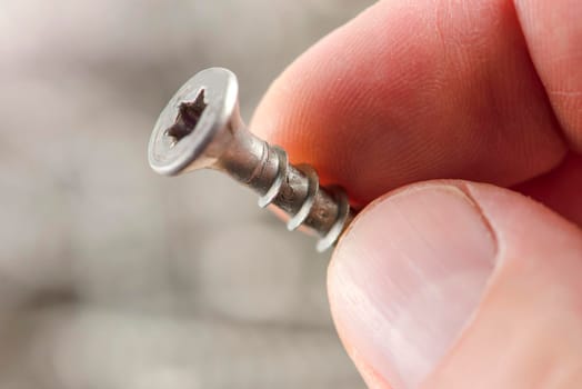 A man holds a screw, close-up. Screws for the production of wooden furniture. Repair and repair tools. Stainless steel bolts