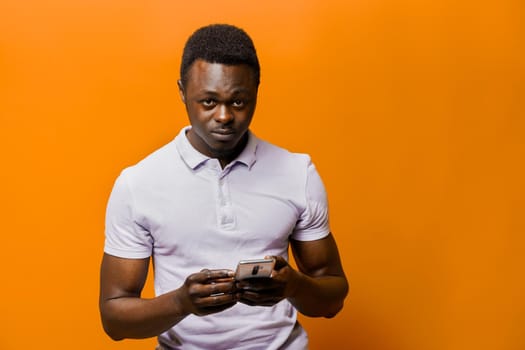 Handsome african with phone on orange background. Business portrait in studio. Online business.