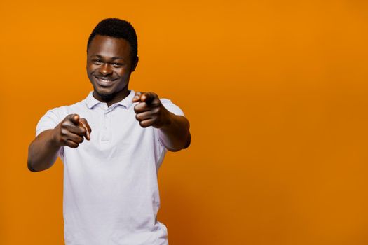 Happy african man points to camera. Motivation from black sportsman. Bearded motivated man on orange isolated background with empty space