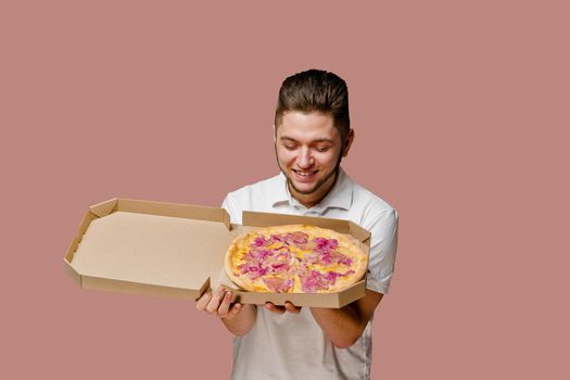 Handsome young happy man sniffs a tasty pizza. Safety on-line delivery at quarantine period. Stay at home and eat a pizza.