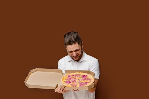 Online pizza safety delivery servise from restaurant. Young surprised courier man sniffs pizza laugh. empty space for advertise.