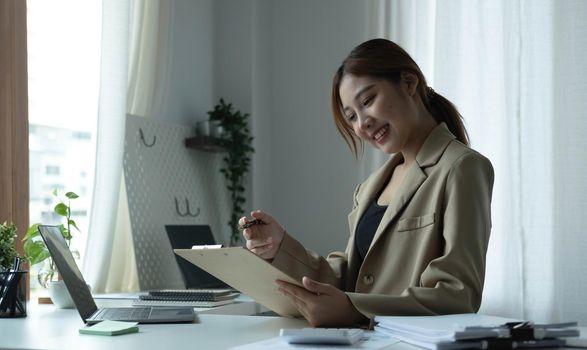 Attractive young woman sitting and her workplace and checking information on clipboard..