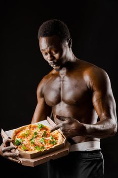 Surprised naked black man points pizza in cardboard box. Advertise for pizzeria. Isolated black backround. Discount for pizza.