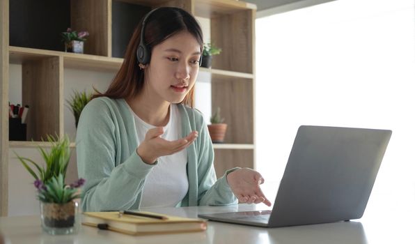 Happy young woman in headphones speaking looking at laptop making notes, girl student talking by video conference call, female teacher trainer tutoring by webcam, online training, e-coaching concept.