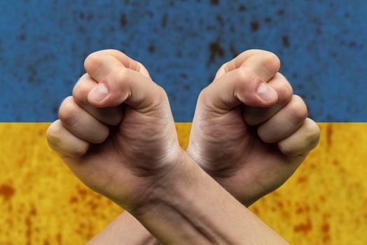 Confrontation and competition. The man crossed his arms over his chest, clenching his fists in front of the Ukrainian flag. The concept of confrontation and struggle.