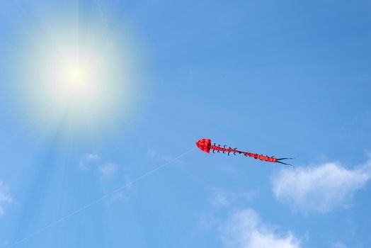 Flying kite. A multi-colored kite is flying in the sky. Blue sky with clouds and sun. Space for text or copy space
