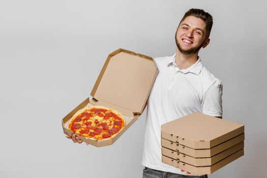 Funny young caucasian courier with pizza and 4 cardboard box with pizzas. Handsome man holds pizza and smiles.