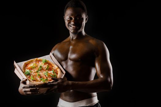 Funny black man with pizza smiles. Undressed african works in safety food delivery. Fit man with food from restaurand. Black undressed man with pizza