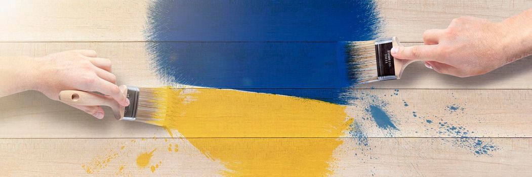 Men's hands with brushes draw a heart in the shades of the Ukrainian flag. Heart in blue and yellow on a wooden background