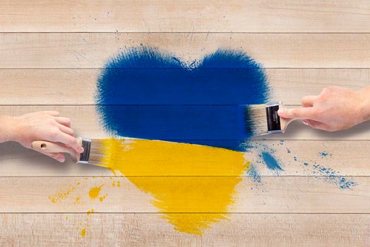 Men's hands with brushes draw a heart in the shades of the Ukrainian flag. Heart in blue and yellow on a wooden background