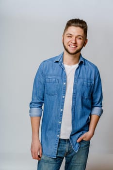 Young handsome man stands over white background and smiles. Confident man wears casual jeans shirt and looks in camera. Bearded business man.