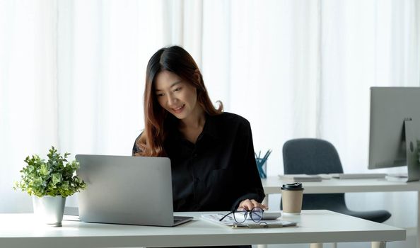 Charming asian businesswoman sitting working on laptop in office..