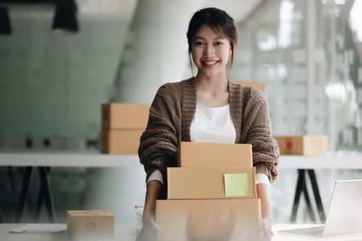 Happy young asian woman startup small business freelance holding parcel box and computer laptop. Online marketing packing box delivery concept.