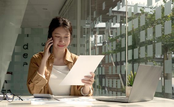 Charming Asian woman with a smile standing holding papers and mobile phone at the office..