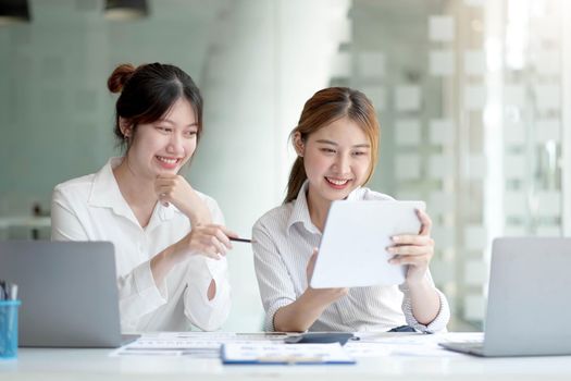 Two young Asian businesswoman discuss investment project working and planning strategy. Business people talking together with laptop computer at office..