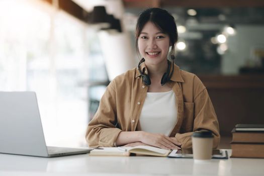 Happy young Asian student woman wearing headphones looking at webcam, looking at camera, during virtual meeting or video call talk..