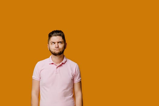 Young handsome man stands over orange background and smiles. Confident man wears pink shirt and looks in camera. Bearded caucasian business man.