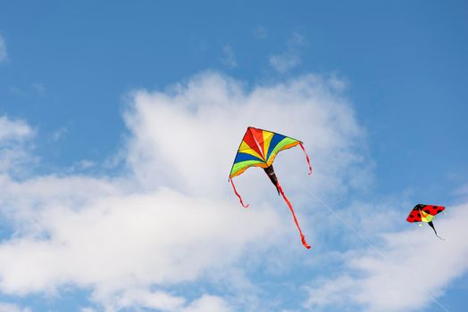 Flying kite. A multi-colored kite is flying in the sky. Blue sky with clouds and sun. Space for text or copy space