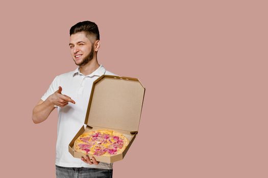 Handsome yound courier with points to pizza. Empty space for text advertise. Safery delivery from restaurant. Confident student works courier