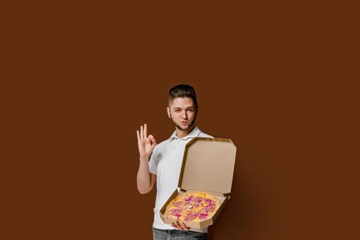 Online pizza safety delivery servise from restaurant. Young caucasian courier man shows ok and smile. Pizza with cheese boards advertise