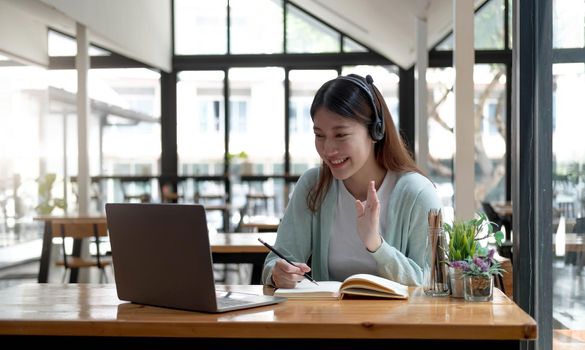 Happy young woman in headphones speaking looking at laptop making notes, girl student talking by video conference call, female teacher trainer tutoring by webcam, online training, e-coaching concept.