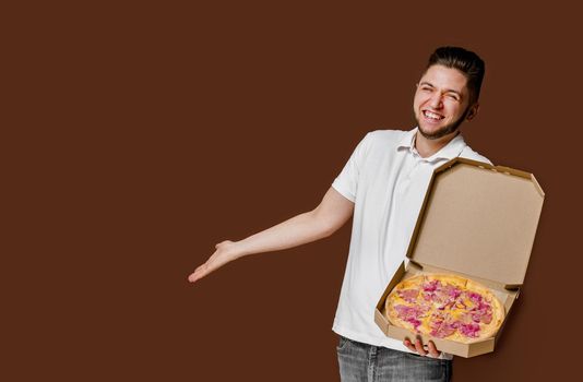 Online pizza safety delivery servise from restaurant. Young surprised courier man smiles and points to empty space for advertise