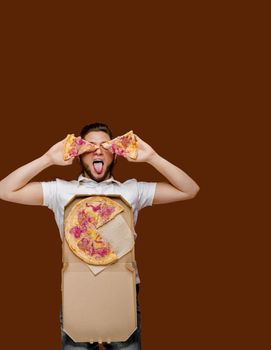 Online pizza safety delivery servise from restaurant. Young handsome courier man lays on brown background and fools around with 2 pieces of pizza.