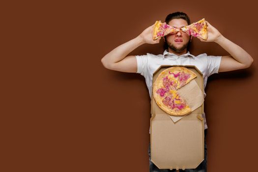 Young handsome caucasian man lays and fools around with 2 pieces of pizza. Creative idea for advertise pizzeria. Surprised young courier