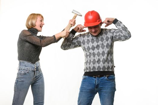 The wife screams and hits her husband on the head with a hammer, the husband is wearing a helmet and he covered his ears with his fingers