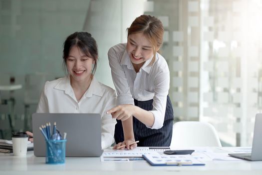 Two young Asian businesswoman discuss investment project working and planning strategy. Business people talking together with laptop computer at office..