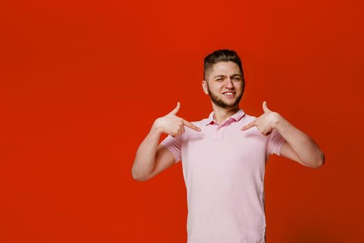 Handsome bearded caucasian man points themself. Confident man wears casual style and stands over red backround. On-line business for students.