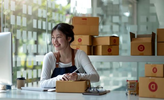 Asian Small business entrepreneur SME writing address on cardboard box at workplace small business entrepreneur SME , working with box at home.