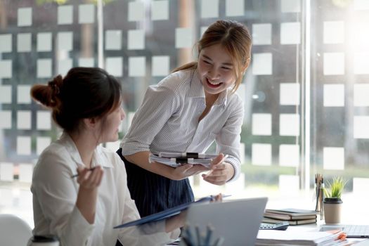 Two hardworking young women entrepreneurs working together on their laptop computers read screens with smiling faces in high angles..