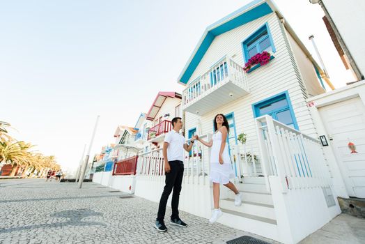 Young couple in white clothes walks around street in Aveiro, Portugal near colourful and peaceful houses. Lifestyle. Having fun, laughs, smiles.