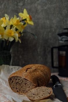 A round loaf of a crusty bread, on a rustic wooden table with scattered flour. Next to it lies a bread knife