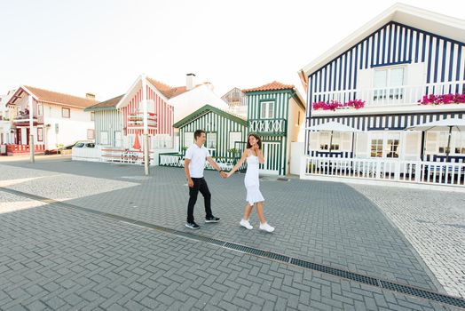 Young couple in white clothes walks around street in Aveiro, Portugal near colourful and peaceful houses. Lifestyle. Having fun and laughs.