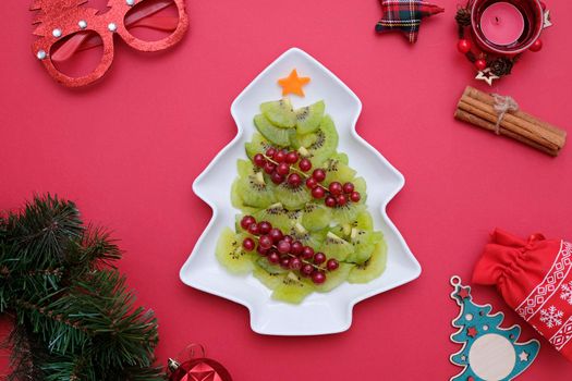 Creative edible vegan christmas tree, food art. Food for kids and festive table. Tree made from kiwi on a white tree plate