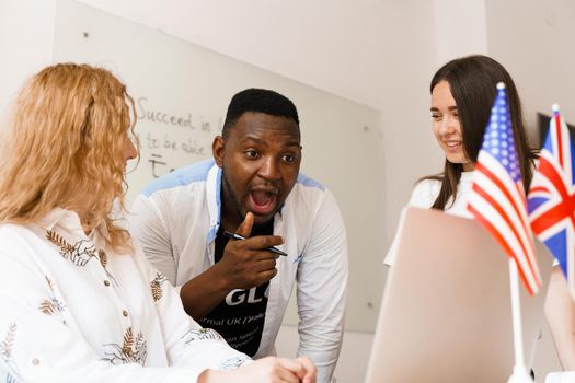 Online multiethnic attractive group of teachers study and laught, discuss something. Remote work in multinational group with laptop.