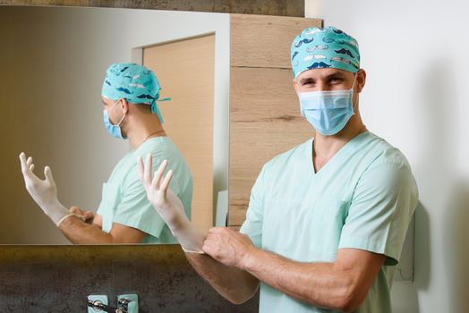 Smile surgeon puts sterile medical gloves on his hands and looks in camera. Protect of pandemic of coronavirus covid 19 Hygiene for hands