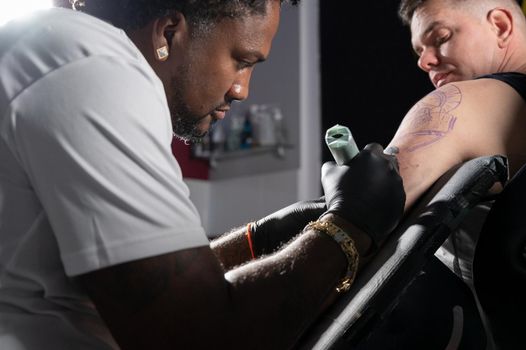 Professional African American tattoo artist makes a tattoo on client arm. High quality photography.